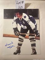 Full view of signed hockey photo featuring David Keon in full uniform on ice, showing autograph and part of hockey stick.