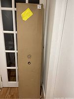 Full view of the cardboard shipping box standing upright against a wall, showing the unopened and intact packaging of the shoe rack.