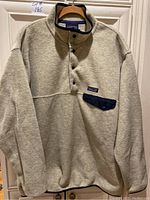 Front view of light grey Patagonia Synchilla pullover fleece top with chest pocket featuring dark flap and Patagonia logo patch.