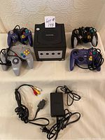 Overhead view of black Nintendo GameCube console with four controllers, AC adapter and composite AV cable.