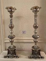 Pair of tall, ornately carved metal candlesticks placed side by side showing full height and symmetrical shape
