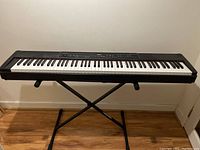 Full view of Yamaha P-90 electronic piano on Ultra Kamman X-stand on wooden floor, no bench visible in this photo.