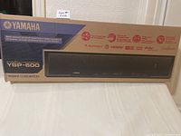 Photo of the Yamaha YSP-600 Digital Sound Projector in its original sealed box showing front and side with branding and features.