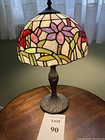 Full view of the lamp showing bronze base and stained glass floral shade, lit to show translucent colors.