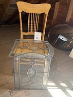 Photo of vintage stained glass windows stacked against a wooden press back chair on wooden floor.
