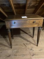 Full front view of small antique ladies desk showing single drawer and turned legs, wood floor beneath.