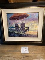 Framed beach scene painting showing two chairs under umbrella at sunset on beach
