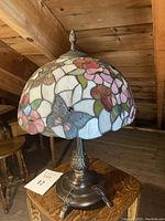 Full lamp showing stained glass floral and butterfly shade with alloy base on wood surface
