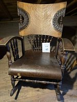 Front full view of antique wooden rocking chair showing pressed oak style backrest with carved details, curved armrests, and turned legs with rockers.