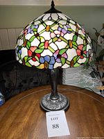 Full view of the stained glass art lamp with floral patterns and multicolor flowers on a white background, standing on a round wood table.