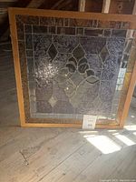 Full view of the square stained glass window insert with its wooden frame placed on a wooden floor.