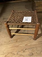 Full view of vintage small wooden stool with woven top, showing four round legs and the woven seat.