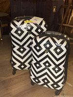 Photo showing the two Heys America hard case suitcases with black and white geometric Art Deco pattern, upright on spinner wheels.