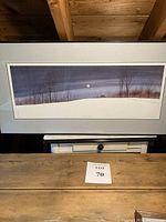 Framed landscape print showing a moonlit winter scene with bare trees and a small building, wide horizontal format.