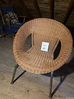 Full view of a round hoop chair with woven natural rattan seat and backrest sitting on metal legs on a wood floor.