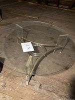 View of full round glass top and supporting acrylic legs with brass braces beneath on wooden floor