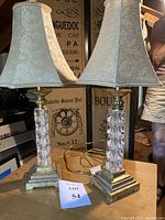 Front view of the two tall lamps showing stacked glass block bases on brass tiered square bases with floral pentagon shaped fabric lampshades.