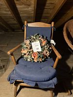 1950s carved maple spring rocker chair with original navy blue cushions and floral wreath on the seat, photographed from front view.