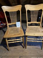 Two antique oak press back chairs with spindle backs and caned seats side by side.
