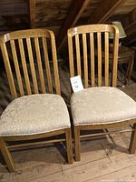 Pair of vintage solid oak chairs with slatted backs and off-white upholstered seats, pictured from front angle.