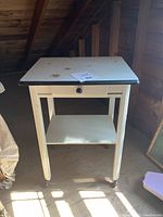 Front view of vintage baking station showing enamel top with black rim, single drawer, off-white painted wooden base, and original wheels.
