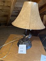 Overall view of the vintage bass table lamp on a wooden surface showing the full lamp and shade with cord visible.