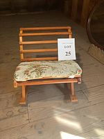 Front view of vintage wooden rocking footstool showing padded floral cushion and wooden slatted frame.