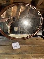 Front view of vintage oval wood framed mirror reflecting rustic room with visible frame condition and reflective surface.