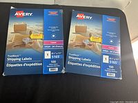 Two unopened packs of Avery TrueBlock shipping labels in blue packaging, each with 100 sheets sized 8.5 x 11 inches, designed for laser and inkjet printers.