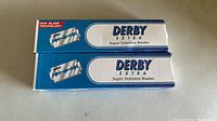 Two boxes of Derby Extra Super Stainless razor blades placed side by side on a surface, showing front packaging.