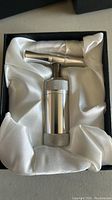 Single heavy duty metal pollen press tool with a screw handle, sitting on a white satin fabric inside a black box.