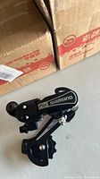 Shimano Tourney RD-TY21 rear derailleur short cage viewed from the side showing the Shimano logo and detail of the derailleur components, placed on a flat surface.