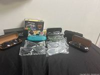 Photo showing multiple pairs of sunglasses and eyeglasses with various cases including a turquoise ZIYENNE case and brown leather-look case on a black cloth surface.