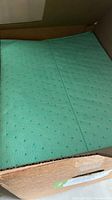 Green heavy duty cleaning pads inside an open cardboard box. The pads are textured and stacked uniformly.