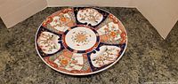 Front view of 12 inch round Asian porcelain serving tray with blue, bronze, and orange floral and traditional patterns.