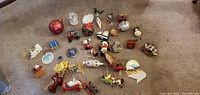 Wide shot of over 30 assorted small Christmas tree ornaments laid out on carpet including Santa Claus, snowmen, trains, sleds, balls, animals, and other holiday-themed decorations.