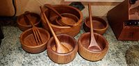 Photo showing a set of seven wooden salad bowls on a kitchen countertop, accompanied by matching wooden salad utensils such as forks and spoons.