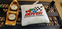 Photo showing a white Dover International Speedway pillow with colorful logo beside a wooden boat-shaped barometer wall hanging with three circular dials.