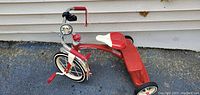 Side view of the red Radio Flyer tricycle showing the front light, bell, handlebars with tassels, white seat, and rear footboard.