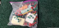 Plastic bag containing Monopoly houses in red and green, dice, paper money bundles, and title deed property cards.