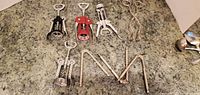 Photo of seven vintage kitchen utensils on a granite countertop: four wing-style corkscrews in various colors and designs; two pairs of metal nutcrackers with spring mechanisms; and a pair of small metal tongs.