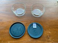 Two clear glass Pyrex bowls with two black plastic lids on wooden surface.