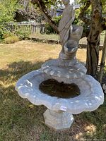 Front view of the three-piece cement fountain in yard, showing figural statue, scalloped bowl, and hexagonal pedestal