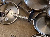 Photo showing four stainless steel pans with handles and matching lids placed on a surface.