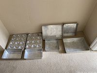 Photo of 8 aluminum baking trays including muffin pans and baking sheets arranged on carpet in a corner