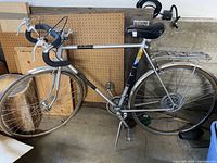 Older Centurion LeMans road bike with drop handlebars and a rear rack, standing indoors with flat tires.