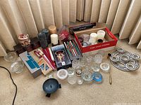 Photo showing various pillar candles in white, cream, and grey, boxed taper candles, multiple clear and colored glass candle holders, and a dark pottery advent candle wreath.