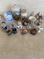 Various small decorative shelf items arranged on carpet, including ceramic jars, figurines, metal cups, and miniatures.