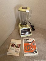 Osterizer blender including base, glass pitcher, and lid. Accompanied by user manual and package of spare seal rings and gaskets.