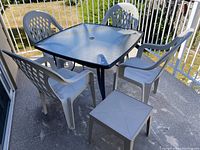 Patio table set on balcony showing square glass-top table with umbrella hole, four white plastic chairs, and one small white plastic side table.
